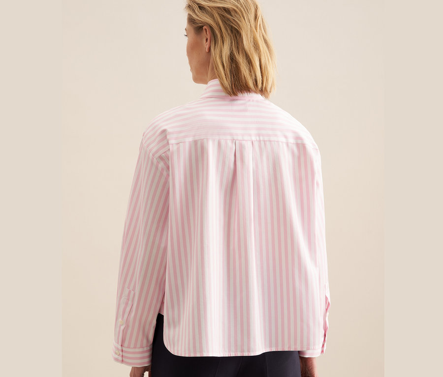 Une femme portant une chemise oversize rose rayée blanche Seidensticker.