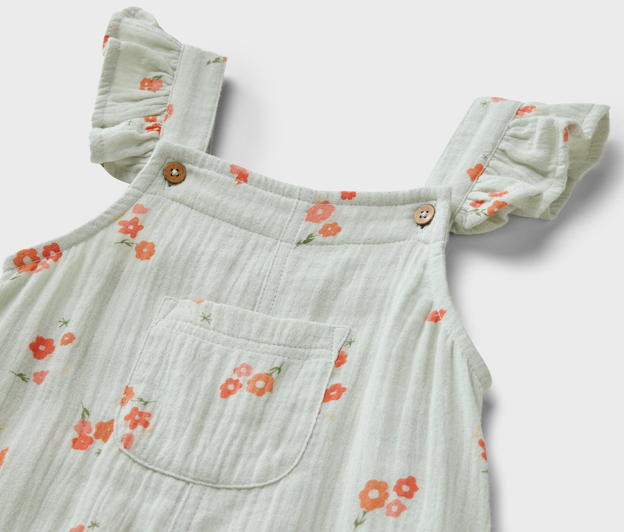 Gros plan sur une barboteuse en mousseline pour enfant, avec un motif floral et des volants sur les bretelles.