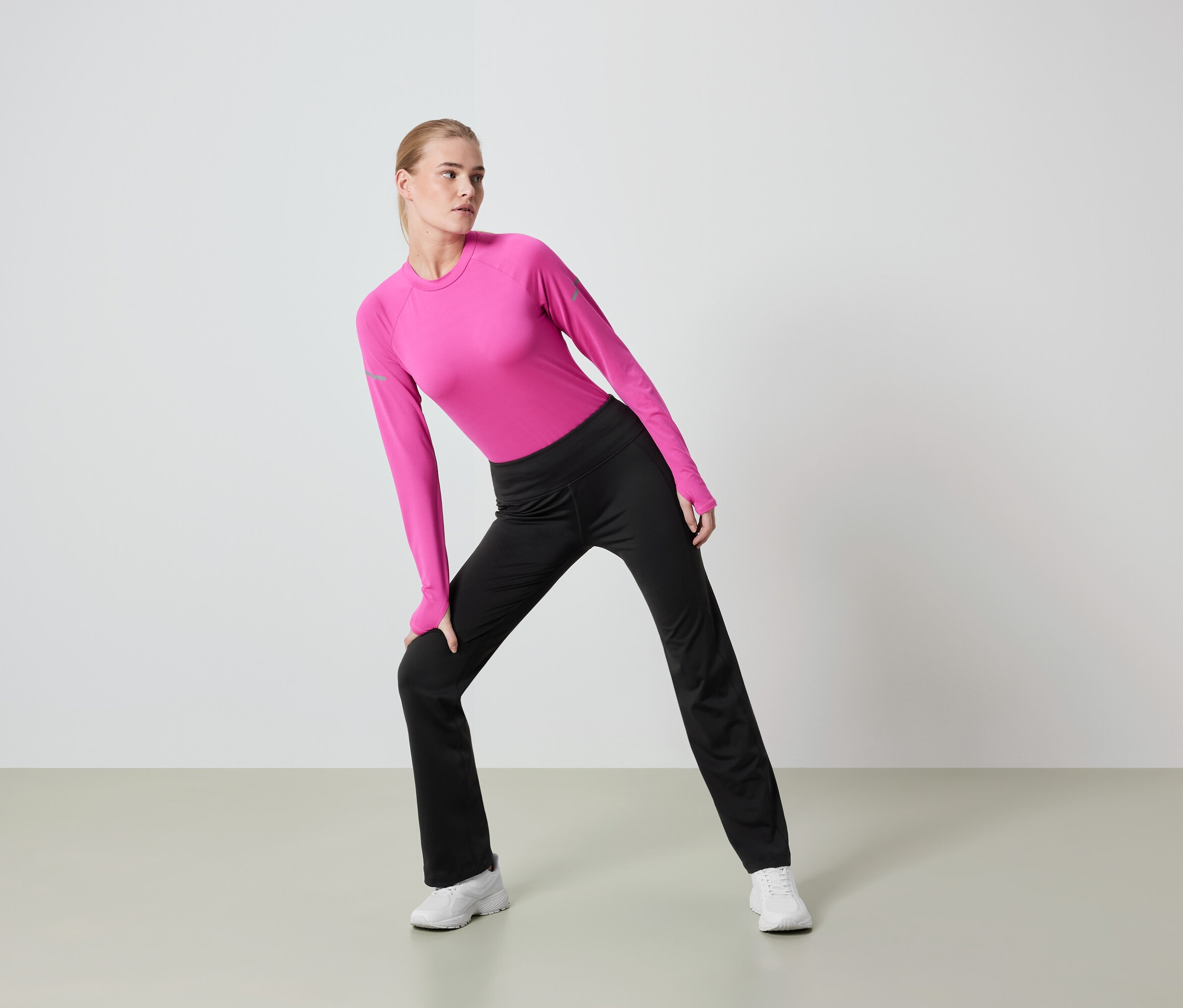 Une femme blonde en legging noir et haut rose à manches longues s'étire.