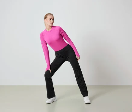 Une femme blonde en legging noir et haut rose à manches longues s'étire.