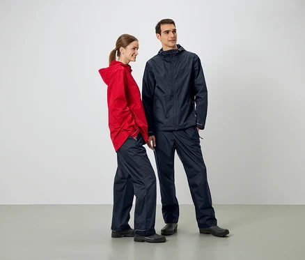 Un homme et une femme se tiennent côte à côte et portent des vestes et des pantalons de pluie.