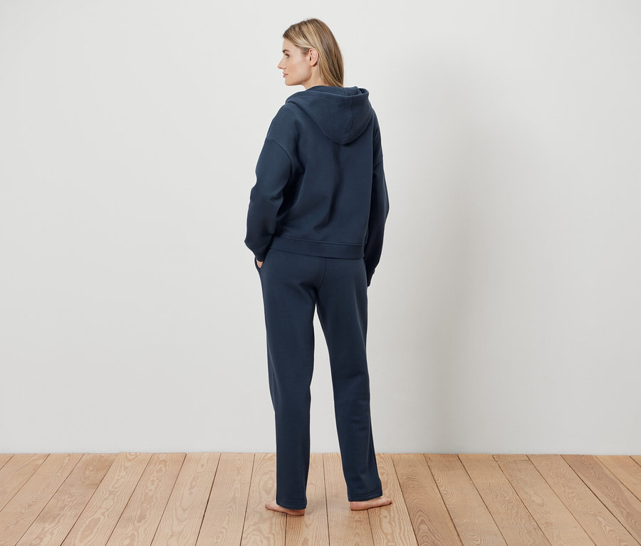 Une femme, vue de dos, porte un sweat à capuche bleu marine et un pantalon de survêtement.