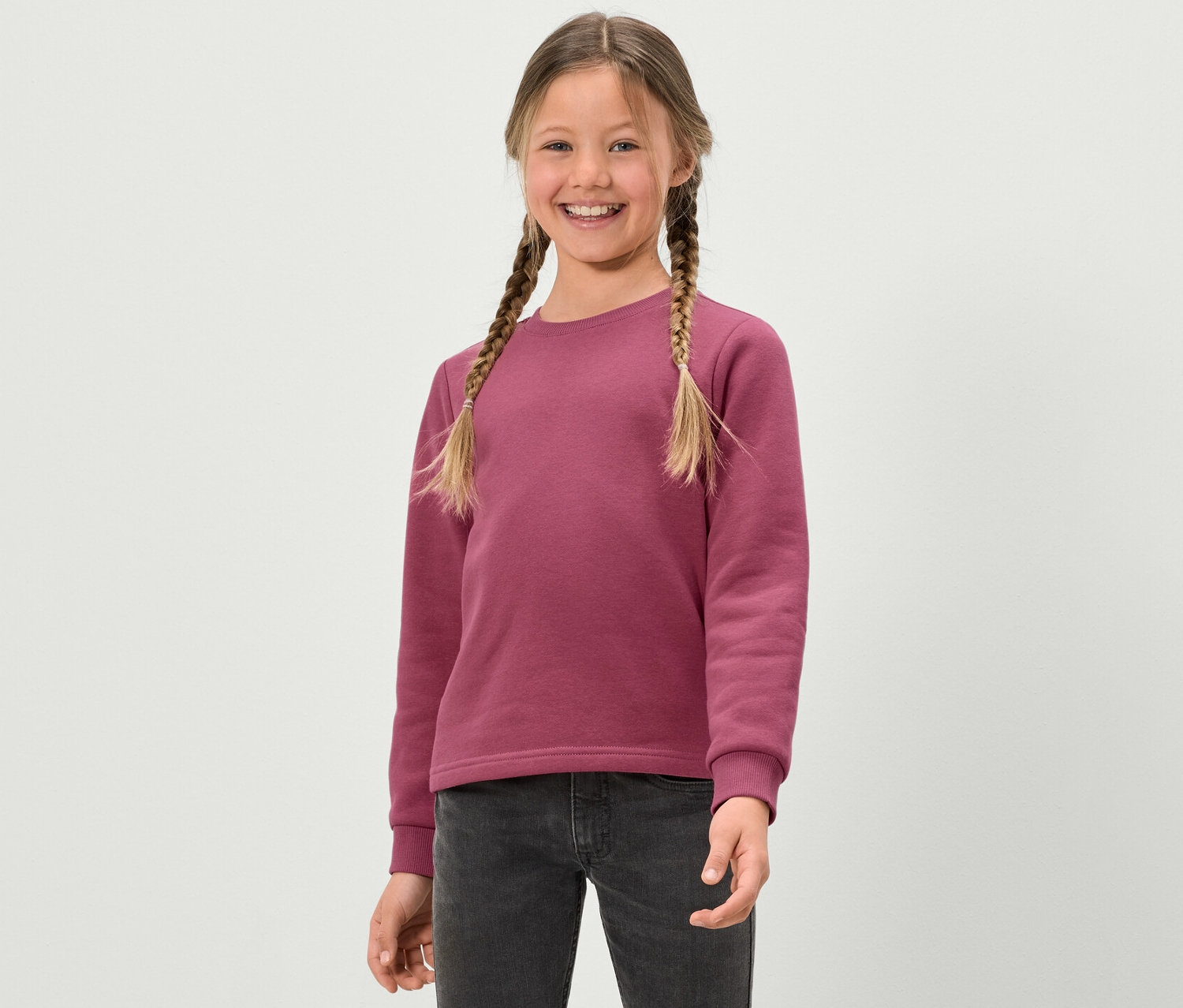 Fillette souriante avec des tresses portant un sweat-shirt rose pour enfants avec un intérieur brossé.