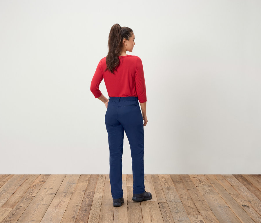 Une femme portant un haut rouge et un pantalon bleu, dos à l'appareil photo.