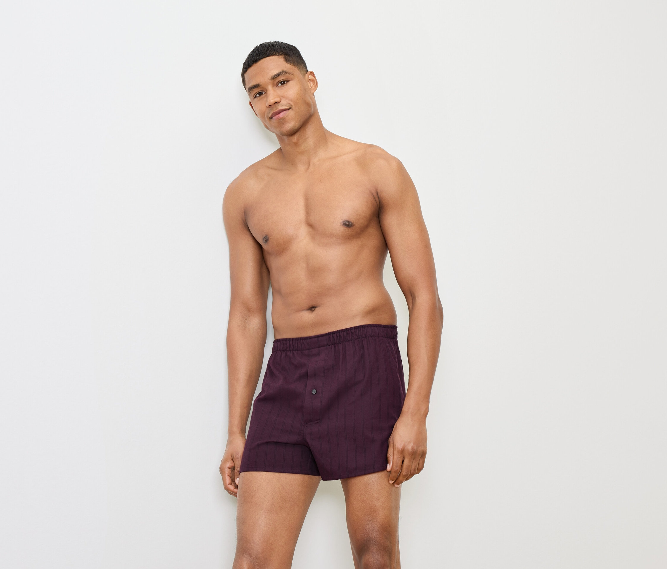 Un homme pose en boxer bordeaux devant un fond blanc.