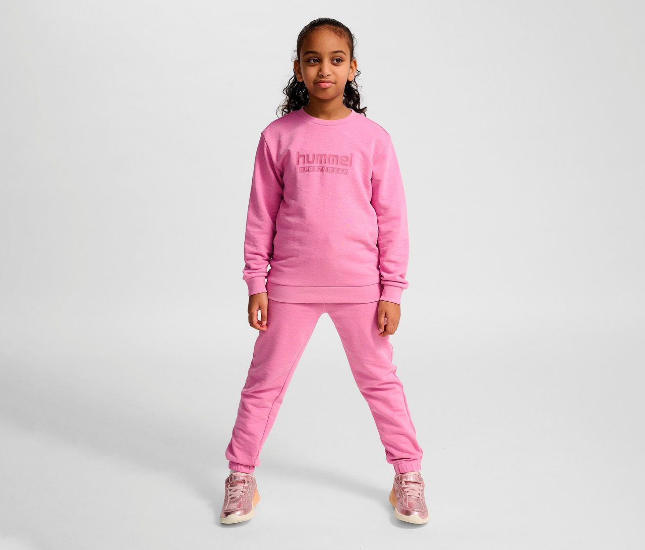 Jeune fille posant dans un sweat-shirt et un pantalon de survêtement roses HUMMEL HMLJR Base.