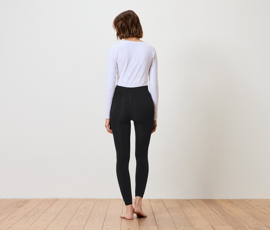 Une femme, vue de dos, porte des leggings noirs et un haut blanc à manches longues.