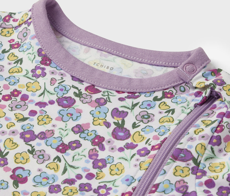Gros plan d'un vêtement de bébé blanc avec des fleurs violettes et jaunes et une bordure violette.