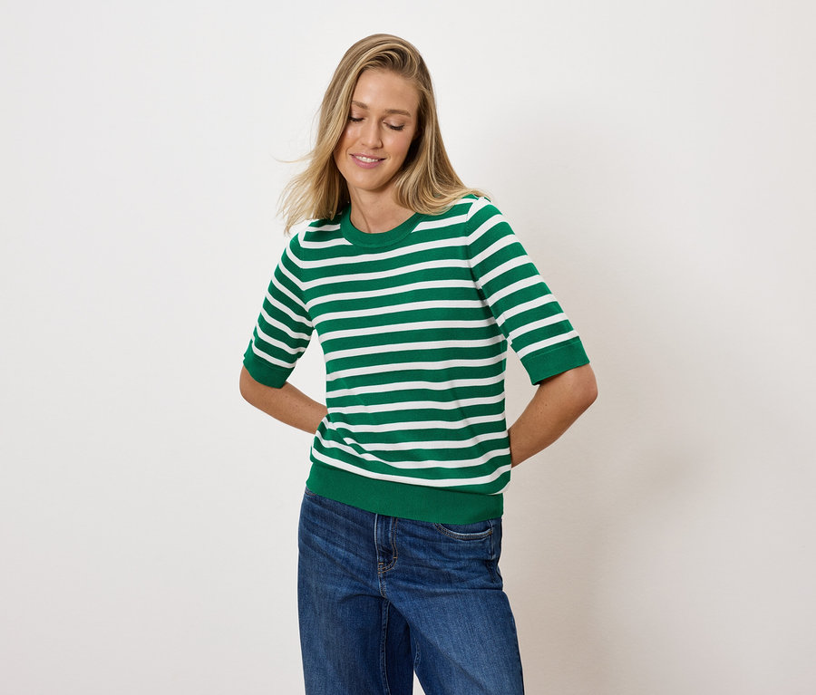 Une femme blonde pose dans un haut rayé vert et blanc et un jean bleu.