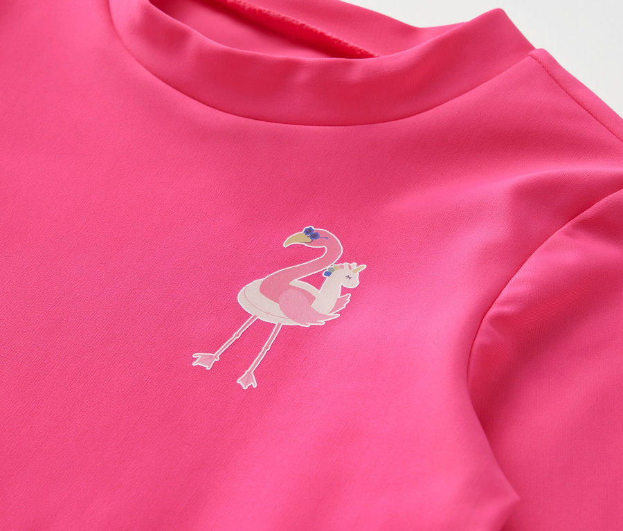 Gros plan sur une combinaison rose pour enfants avec un indice de protection UV 80 et un imprimé flamant rose.