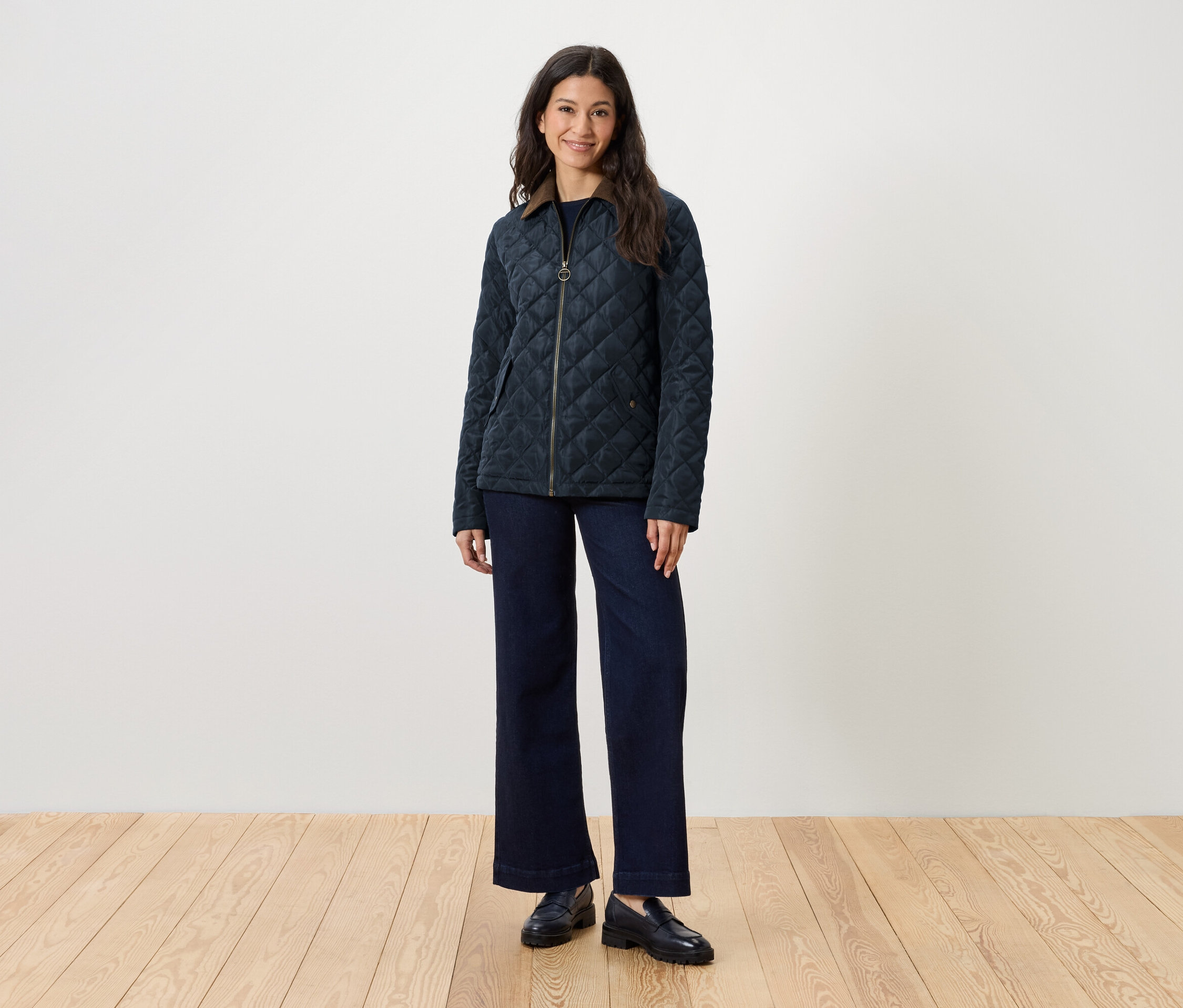 Une femme se tient debout et porte une veste matelassée, un jean et des mocassins.
