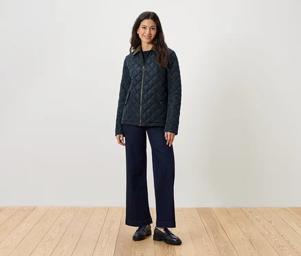 Une femme se tient debout et porte une veste matelassée, un jean et des mocassins.