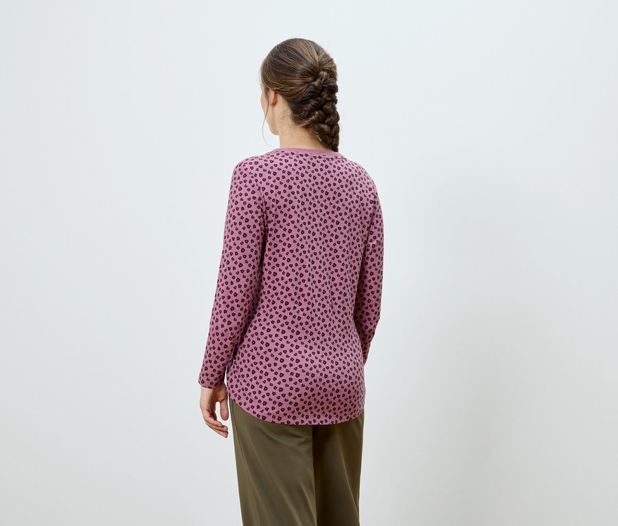 Vue de dos d'une femme avec une tresse brune, portant un haut rose à manches longues avec un motif foncé et un pantalon kaki.