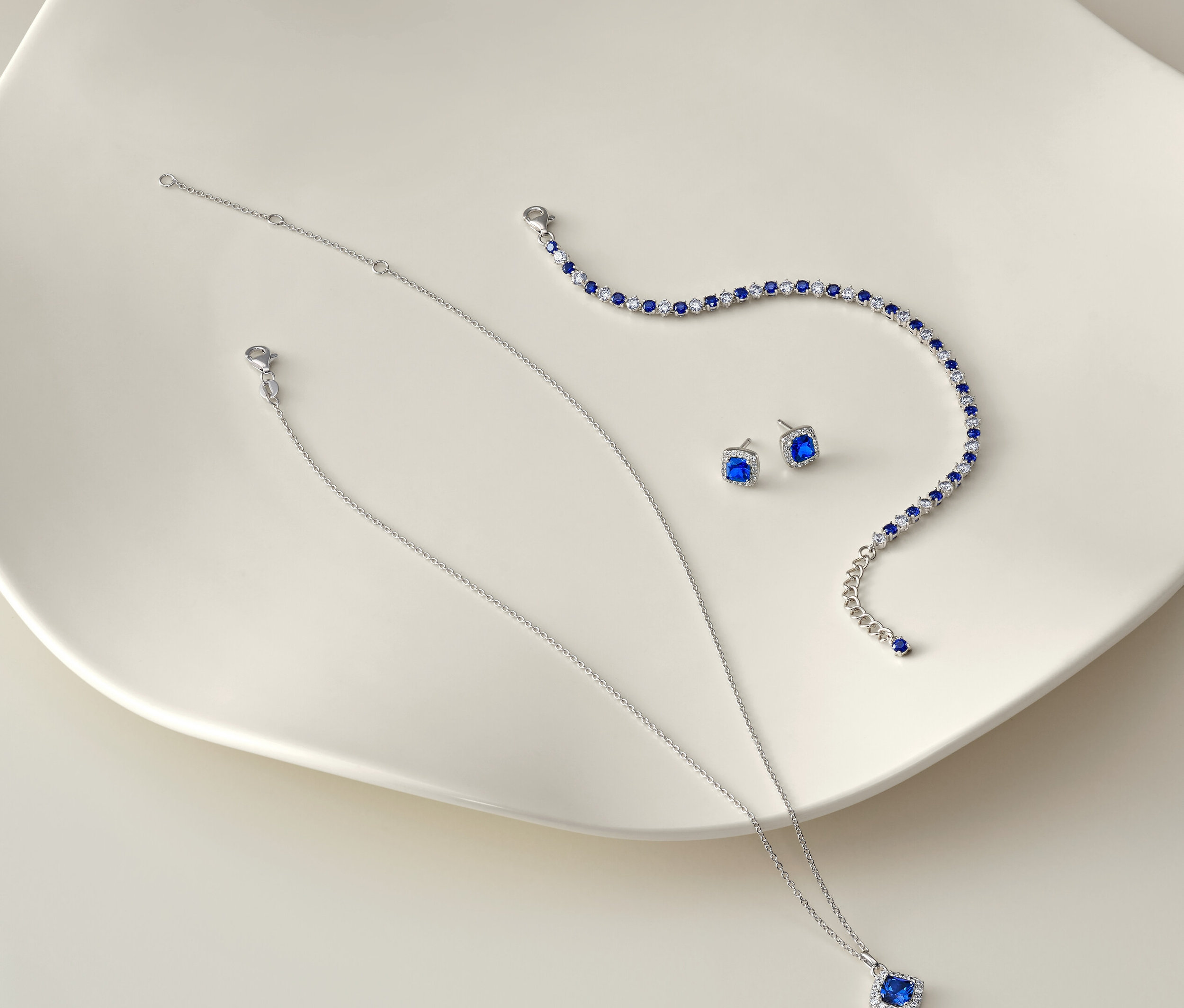 Collier, bracelet et boucles d'oreilles argentés avec des pierres bleues sur fond blanc.
