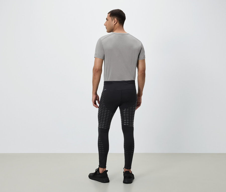 Un homme vu de dos porte un t-shirt gris, un legging noir avec des carrés réfléchissants et des baskets noires.