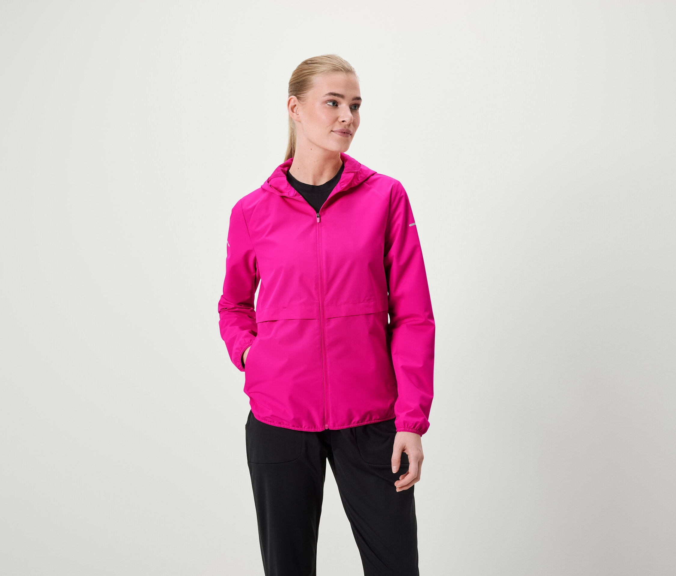 Une femme porte une veste à capuche rose et un pantalon noir.