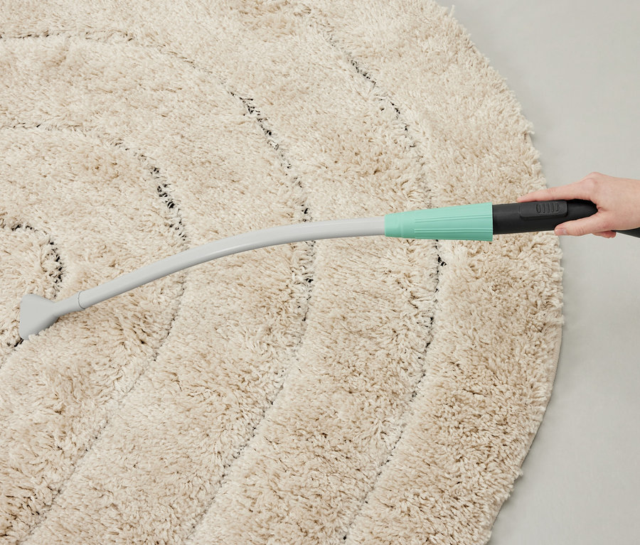 Une personne aspire un tapis rond avec un embout d'aspirateur.