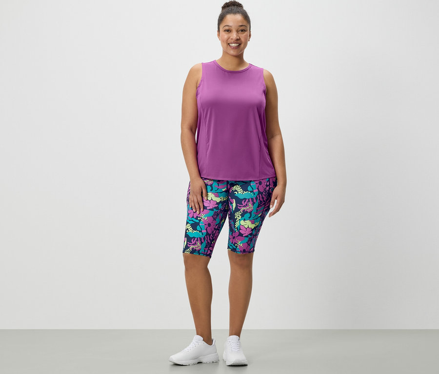 Une femme debout porte un cycliste de sport imprimé intégral et un débardeur de sport turquoise d'un ensemble de 2.