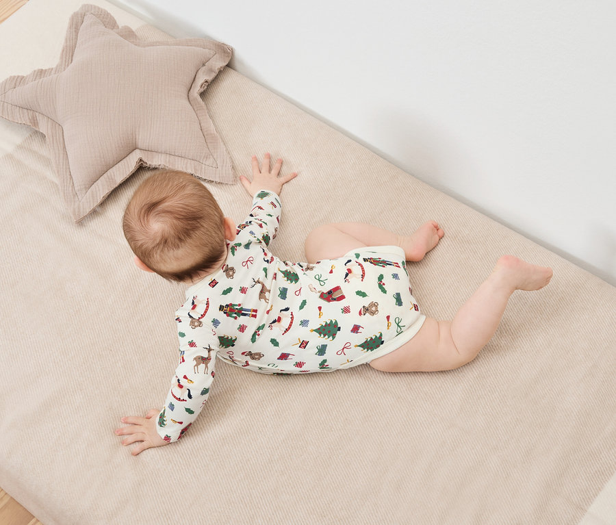 Un bébé est allongé sur le ventre sur une couverture à motifs de Noël à côté d'un coussin beige en forme d'étoile.