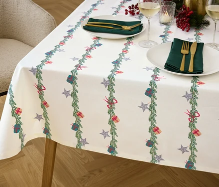 Gros plan d'une table avec une nappe de Noël, des assiettes, des couverts et des verres.