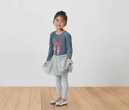 Fillette en tenue de ballet grise avec t-shirt, jupe et leggings.