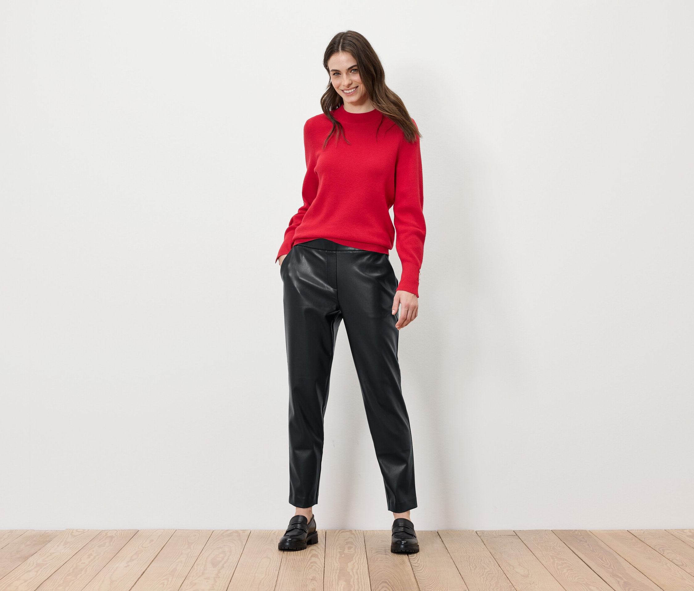 Une femme pose en pull rouge et pantalon en cuir noir.