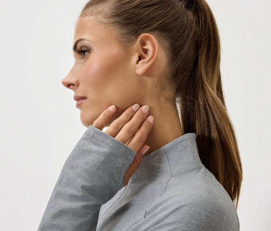 Profil d'une femme aux cheveux brunsQueue de cheval touchant son cou avec une main dans un pull gris.