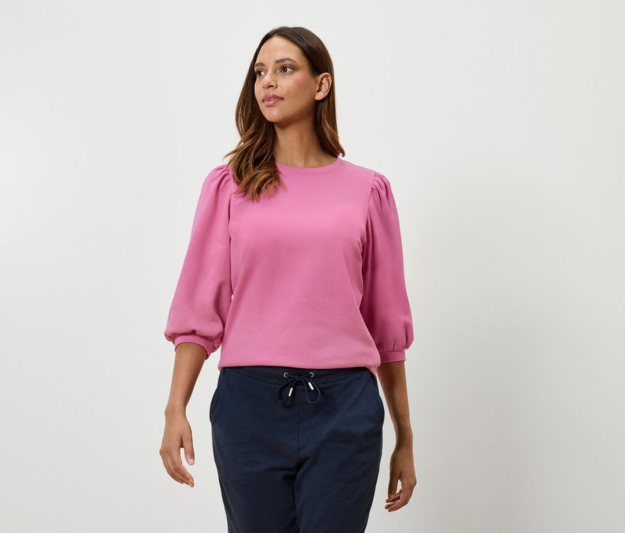 Une femme porte un sweat-shirt rose à manches ballon trois-quarts et un pantalon bleu marine.