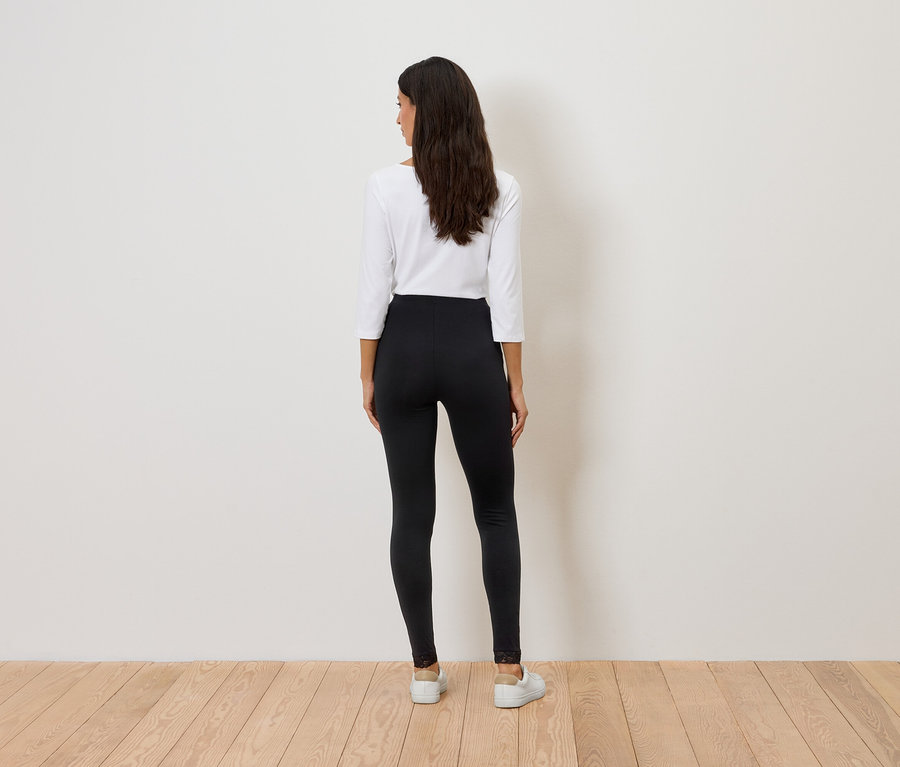 Vue de dos d'une femme aux longs cheveux foncés, portant un haut blanc et un legging noir avec des finitions en dentelle.