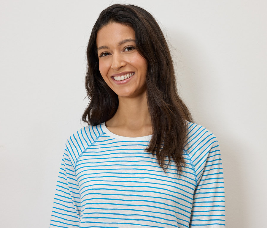 Une femme souriante portant un t-shirt à manches longues rayé bleu et blanc sur un fond blanc.
