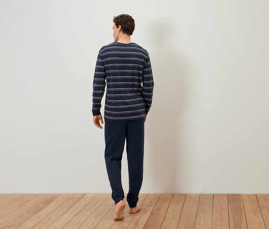 Un homme en pyjama rayé marche pieds nus sur un plancher en bois.