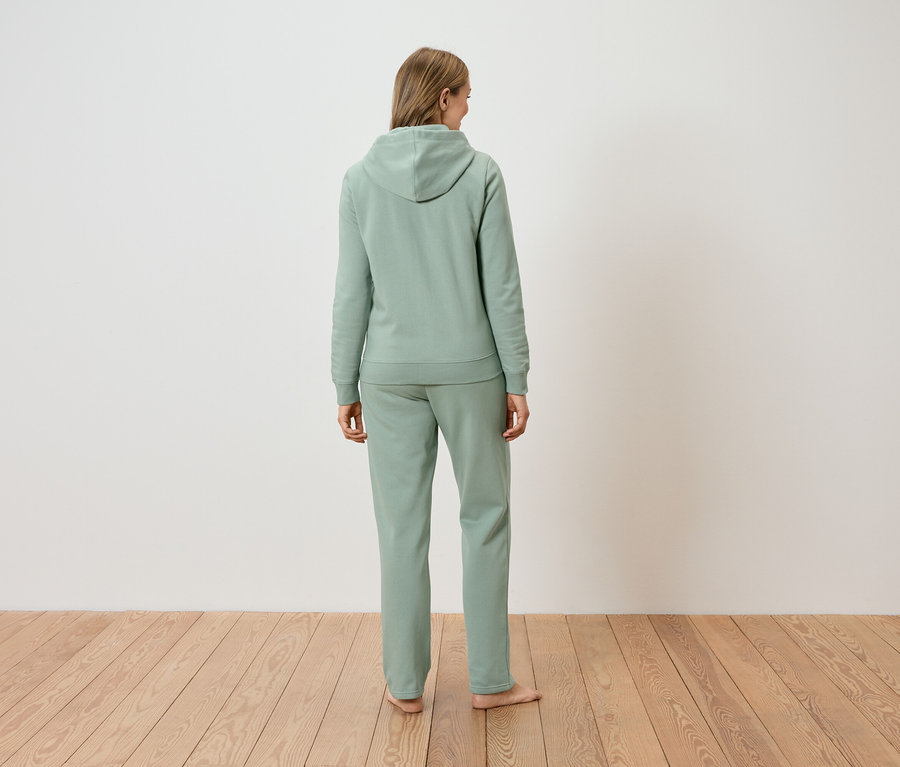 Vue de dos d'une femme aux longs cheveux blonds vêtue d'un sweat à capuche vert clair et d'un pantalon assorti.