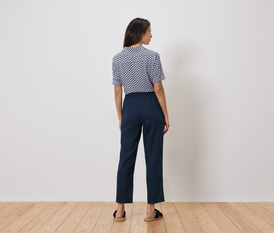 Une femme se tient dos à la caméra, portant un haut bleu et blanc et un pantalon bleu marine.