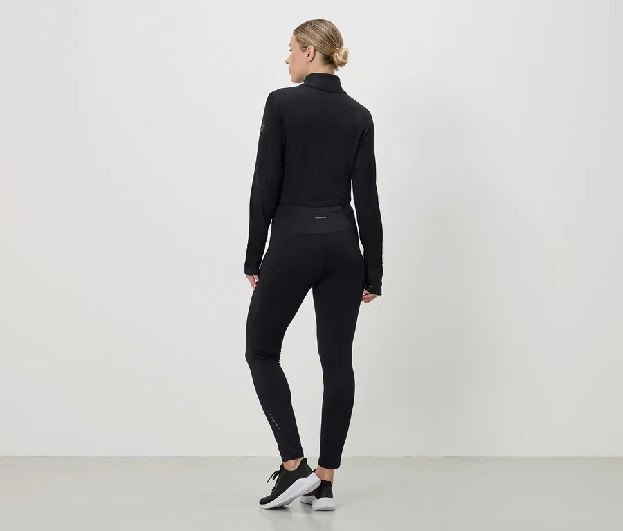 Femme vue de dos portant une tenue de sport noire composée d'un haut, de leggings et de baskets sur fond blanc.