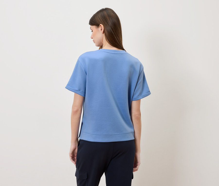 Vue arrière d'une femme aux longs cheveux bruns portant un t-shirt bleu et un pantalon bleu marine.