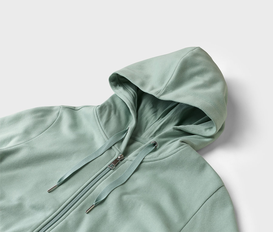 Gros plan d'un sweat-shirt à capuche vert clair avec fermeture éclair sur fond blanc.