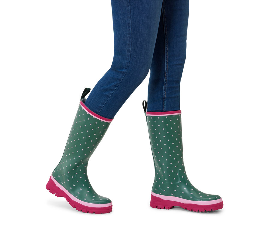 Personne portant un jean bleu et des bottes en caoutchouc vertes avec une semelle rose et des pois blancs.