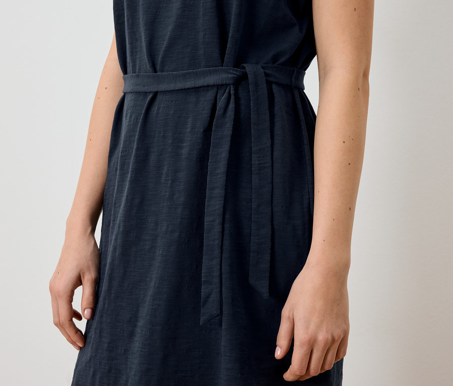 Gros plan d'une femme portant une robe bleu marine sans manches avec une ceinture en tissu.