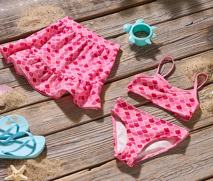 Vue de dessus d'un ensemble de bikini sirène rose, d'une jupe, d'une pelle, de tongs et d'un moule à sable tortue sur du bois.