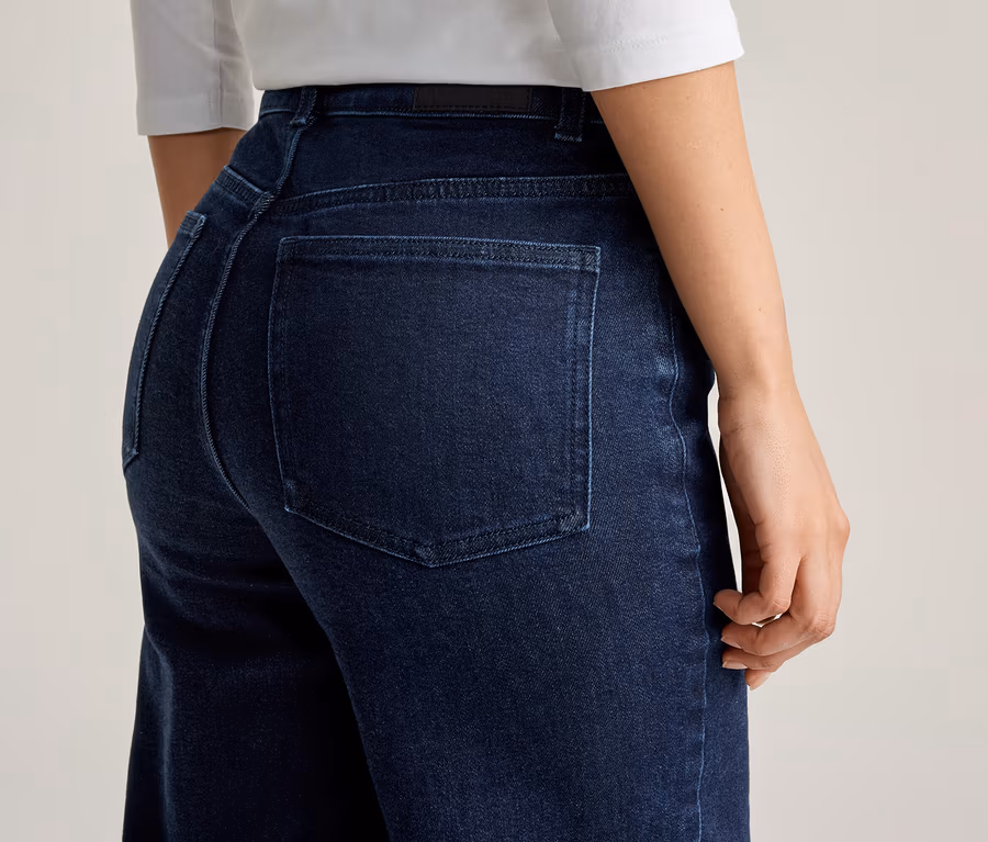 Gros plan d'une femme portant un jean bleu foncé et un haut blanc, photographiée de dos.