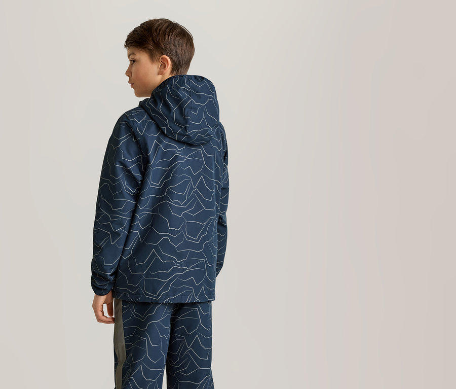 Un garçon se tient debout, portant un sweat à capuche bleu marine et un pantalon assorti avec un motif de montagne blanc.