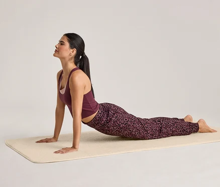 Femme en tenue de sport faisant du yoga sur un tapis beige, en posture du cobra.