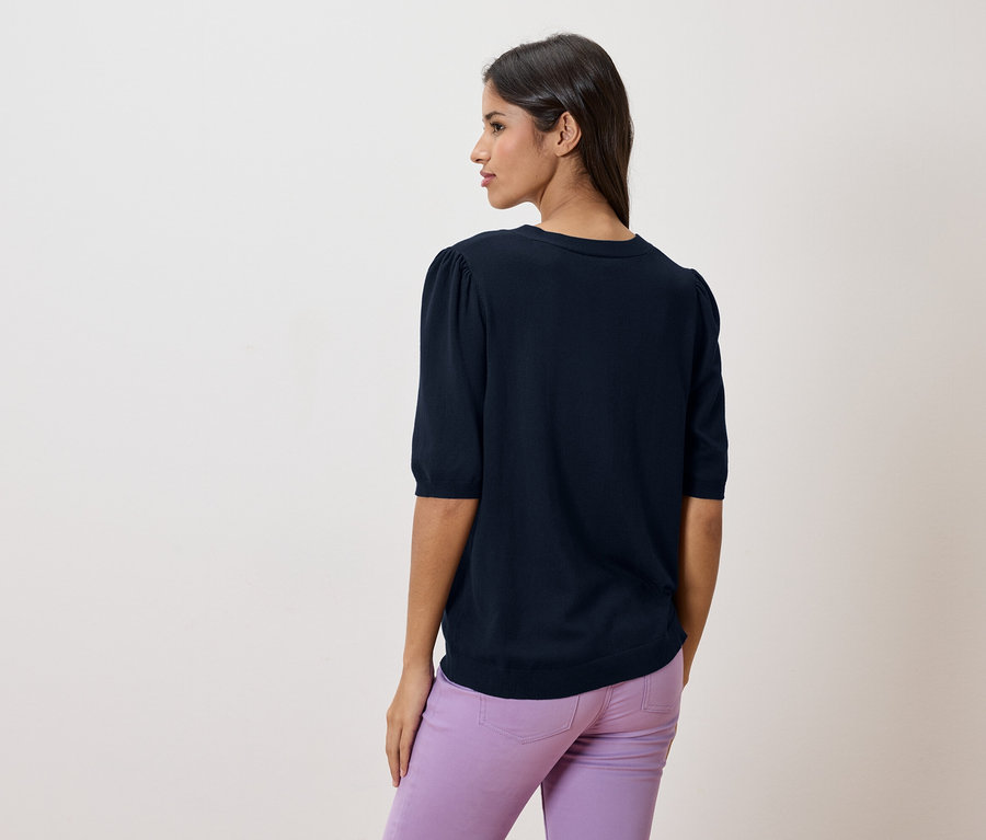 Vue arrière d'une femme aux cheveux foncés portant un pull bleu marine et un pantalon violet.