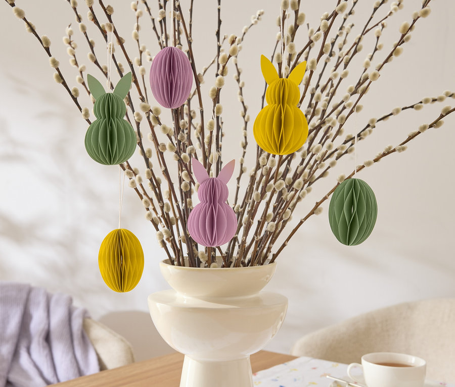 Branches de Pâques décoratives avec des décorations en papier suspendues en forme de lapins et d'œufs en jaune, vert et violet dans un vase.