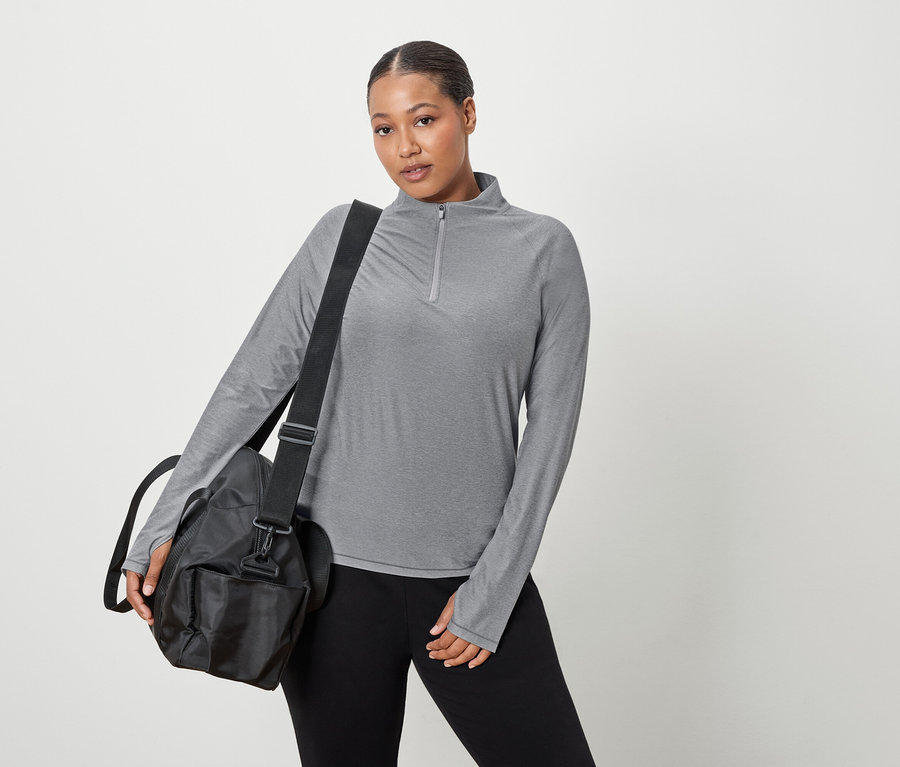 Une femme porte un haut gris à manches longues et un sac de sport noir sur l'épaule.