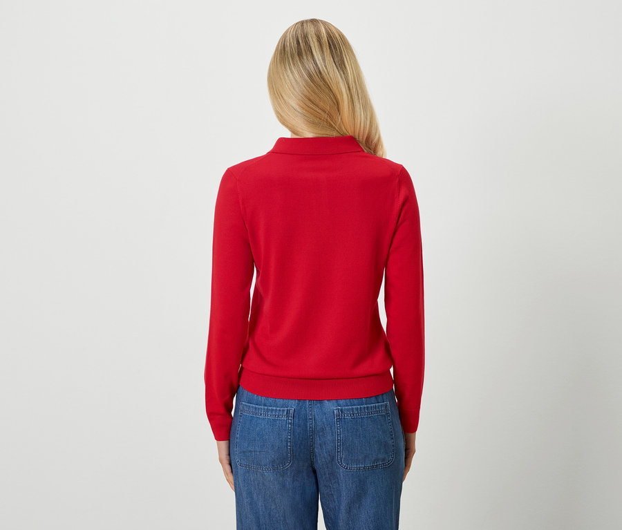 Vue arrière d'une femme aux cheveux blonds portant un pull rouge et un jean bleu.