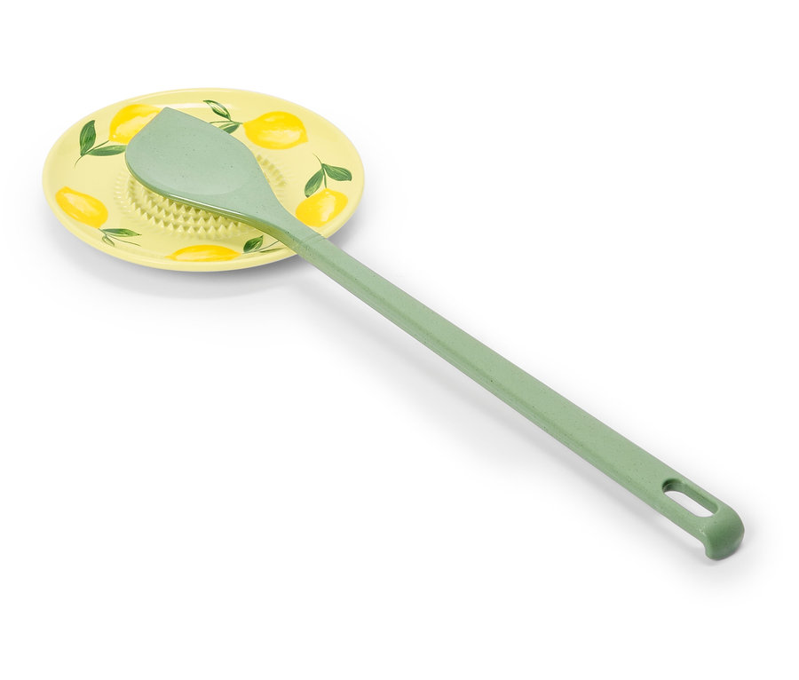 Une cuillère de cuisine vert clair est posée sur un dessous de plat jaune avec un motif de citron.