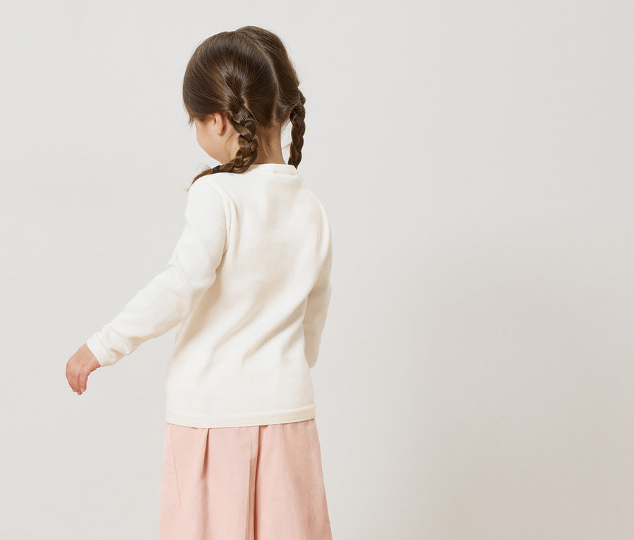 Vue de dos d'une petite fille avec des tresses portant un pull blanc et une jupe rose.