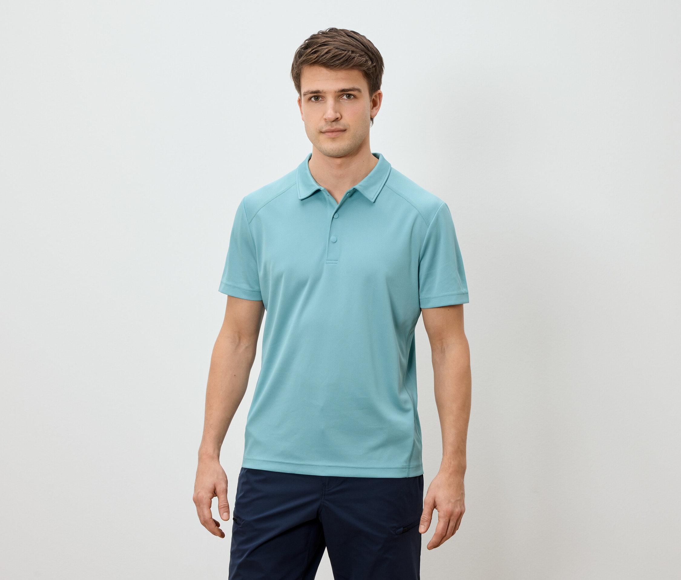 Un homme debout sur un fond clair portant un polo bleu clair et un short bleu marine.