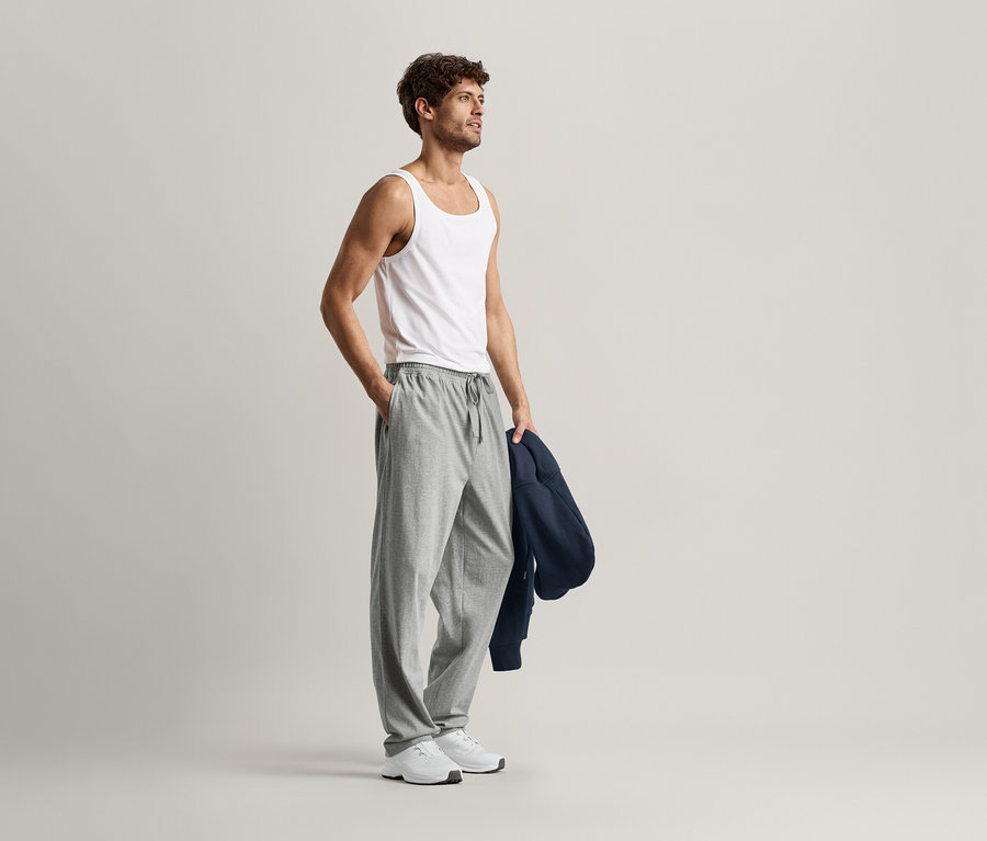 Homme portant un débardeur blanc et un pantalon relax gris.